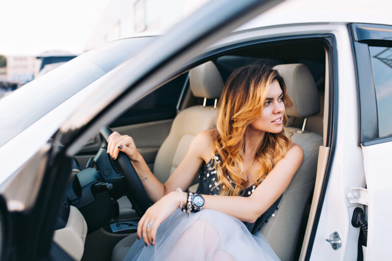 Beautiful model in tulle skirt driving a car. She is looking to side.