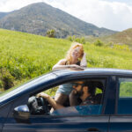 woman-looking-camera-putting-hands-roof-out-car-window