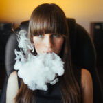 Young beautiful girl exhaling smoke from a hookah and looking at the camera