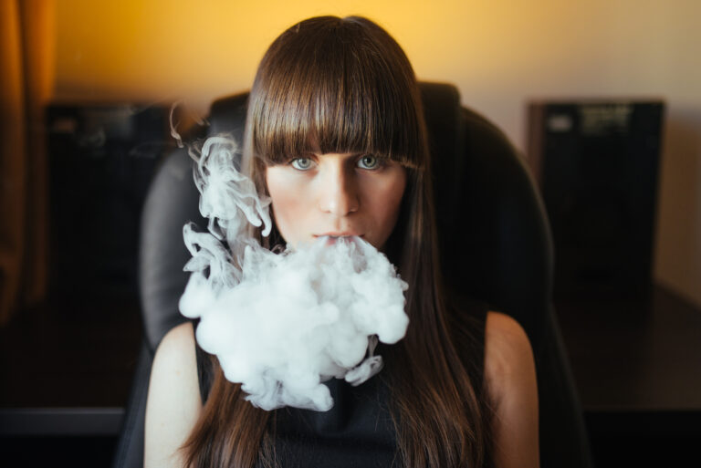 Young beautiful girl exhaling smoke from a hookah and looking at the camera
